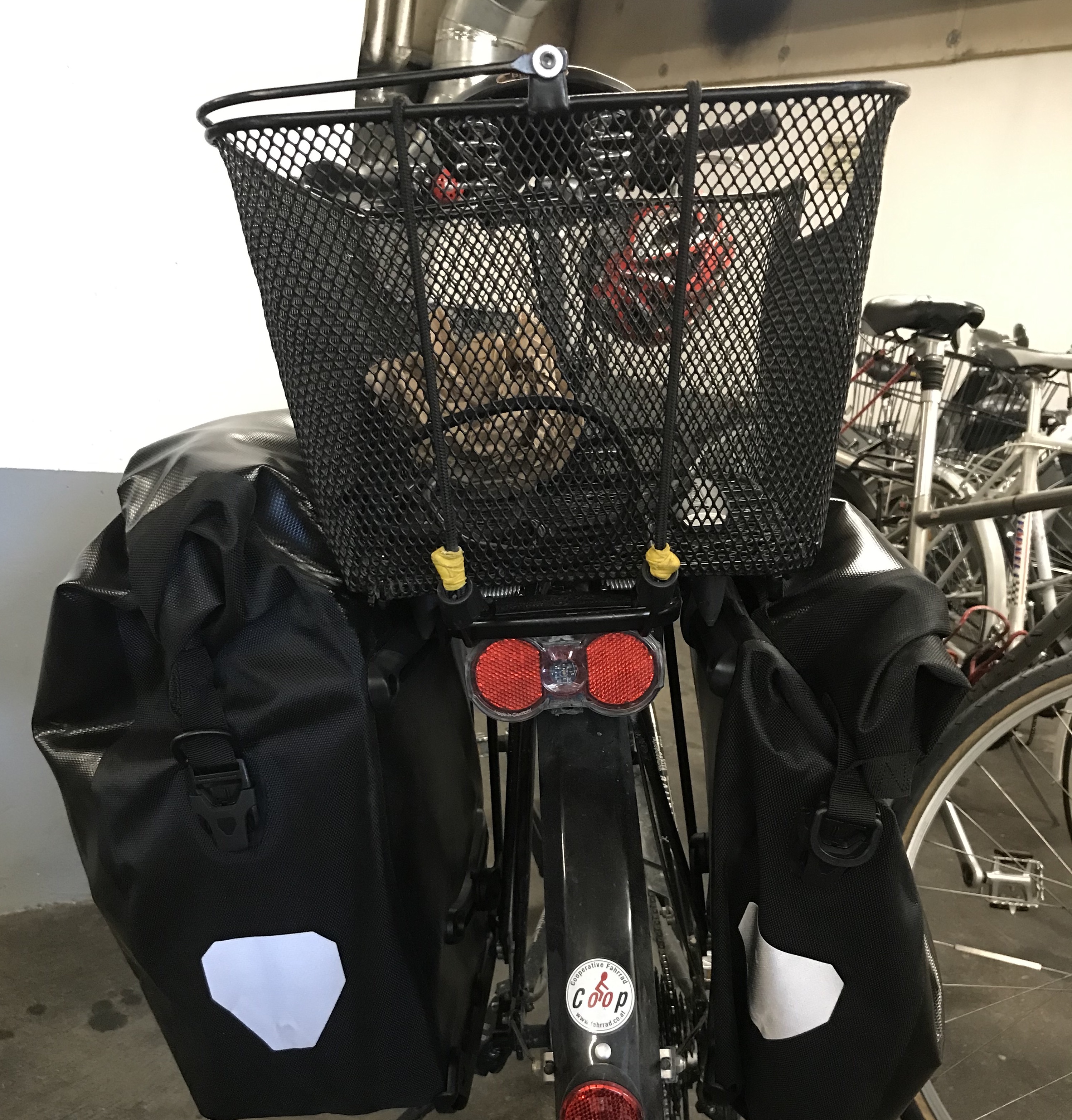 Fahrrad im Ausschnitt von hinten. Links und rechts zwei Packtaschen – oben ein Korb.