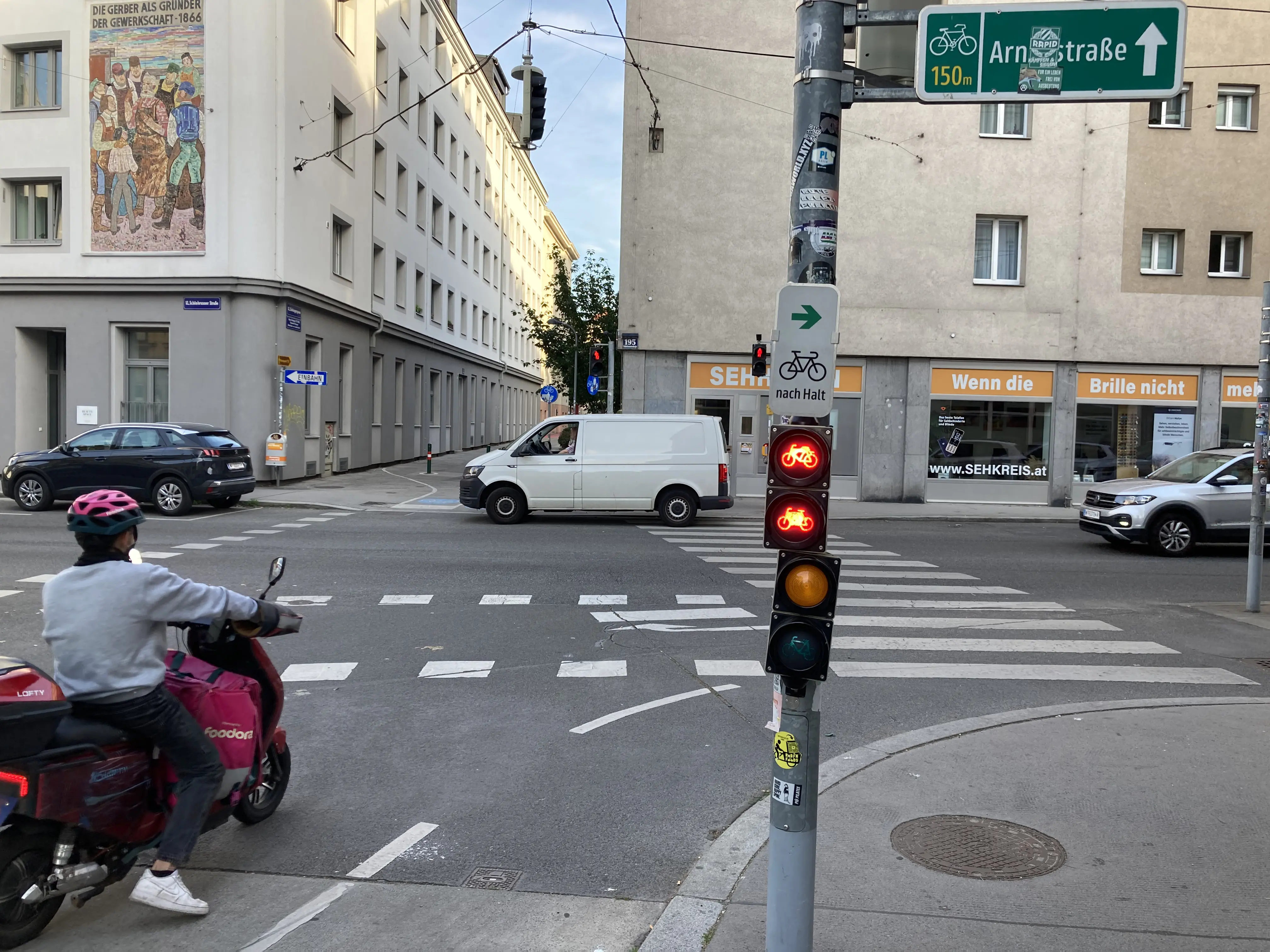 Farbfoto: Mehrkammer-Radampel an einem Mast an einer Kreuzung, daneben Schutzweg und Radquerung